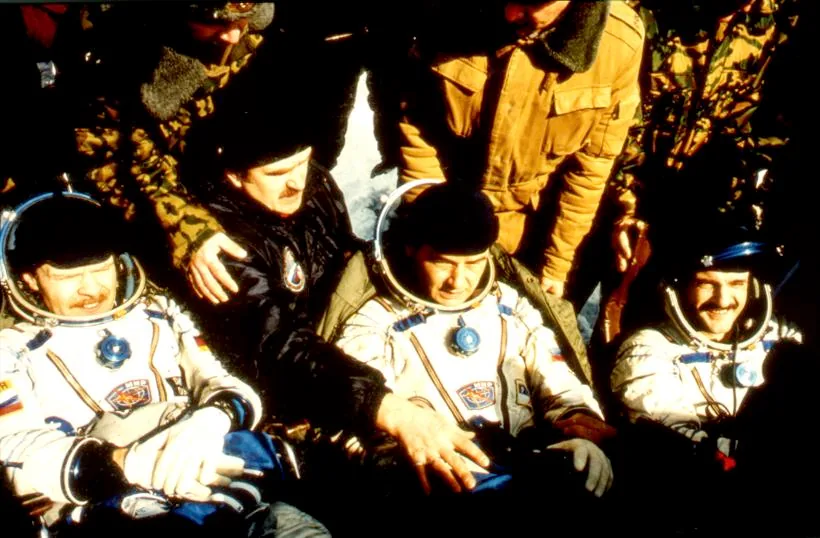 Soyuz TM-24 crew members Valery Korzun, Alexander Kaleri, and Reinhold Ewald seated in pressure suits among recovery personnel after landing in Kazakhstan
