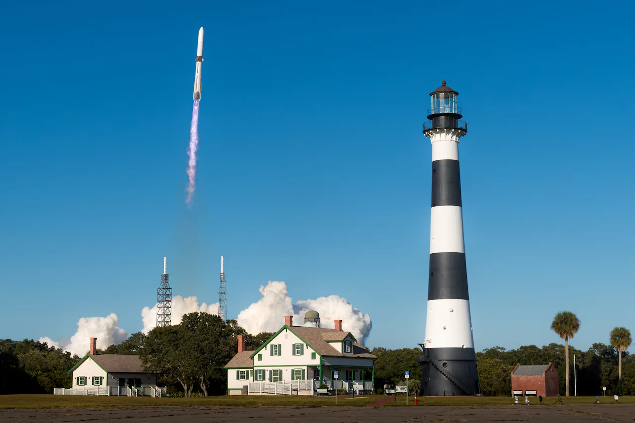 New Glenn climbs through a blue sky beyond the black-and-white Cape Canaveral Lighthouse