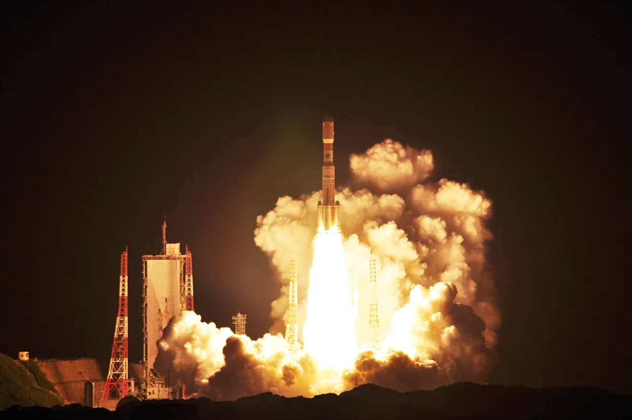H-IIB rises above Tanegashima at night, with a bright exhaust plume and illuminated clouds around the launch towers.