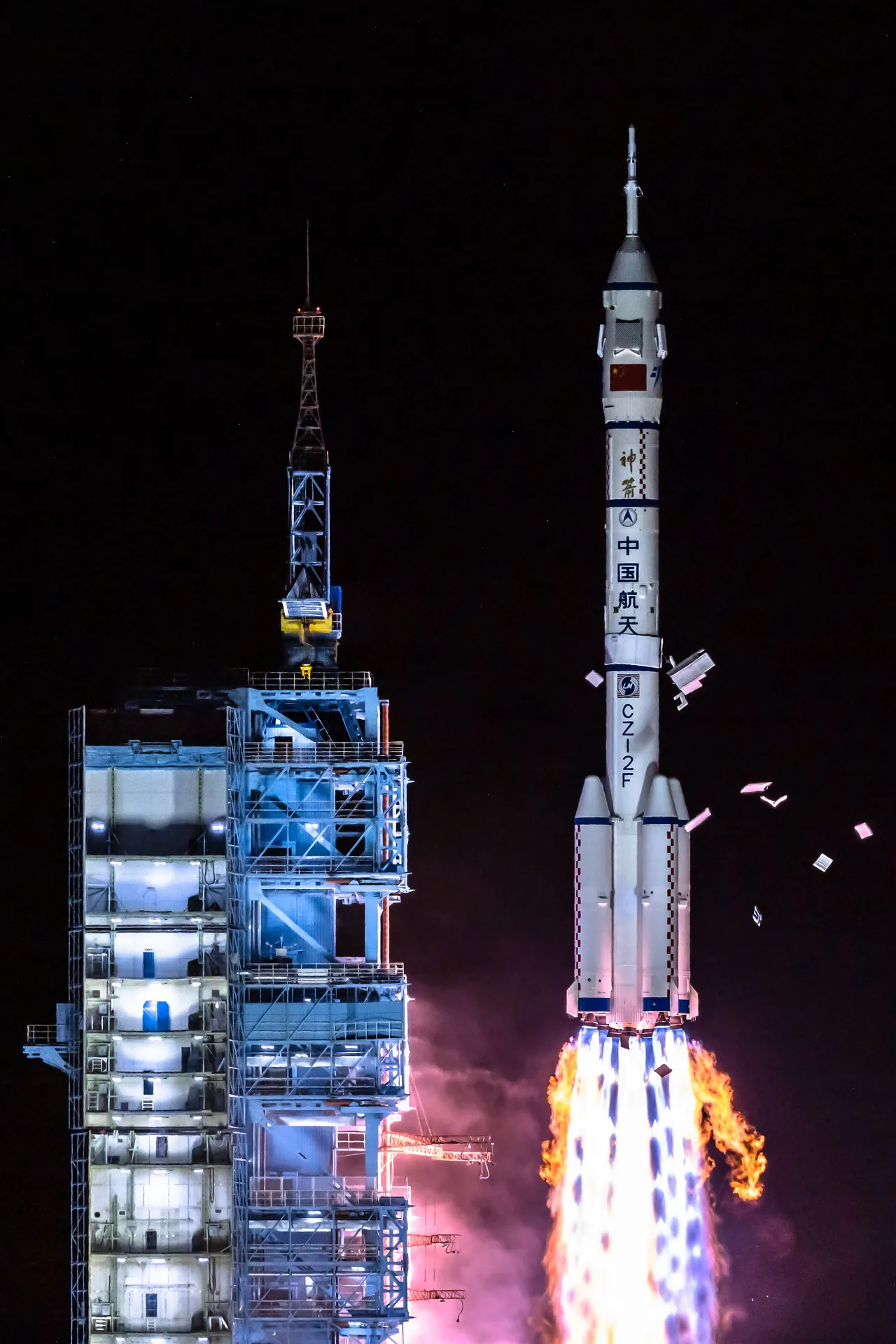 The Long March 2F carrying Shenzhou 13 rises beside the launch tower at night