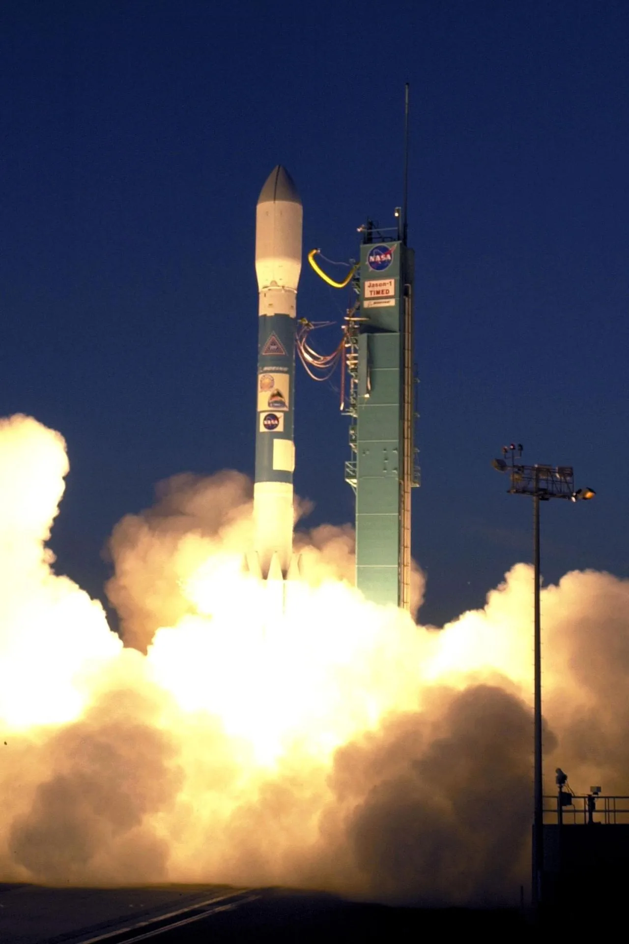 A Delta II rises beside its launch tower with bright exhaust beneath the payload fairing