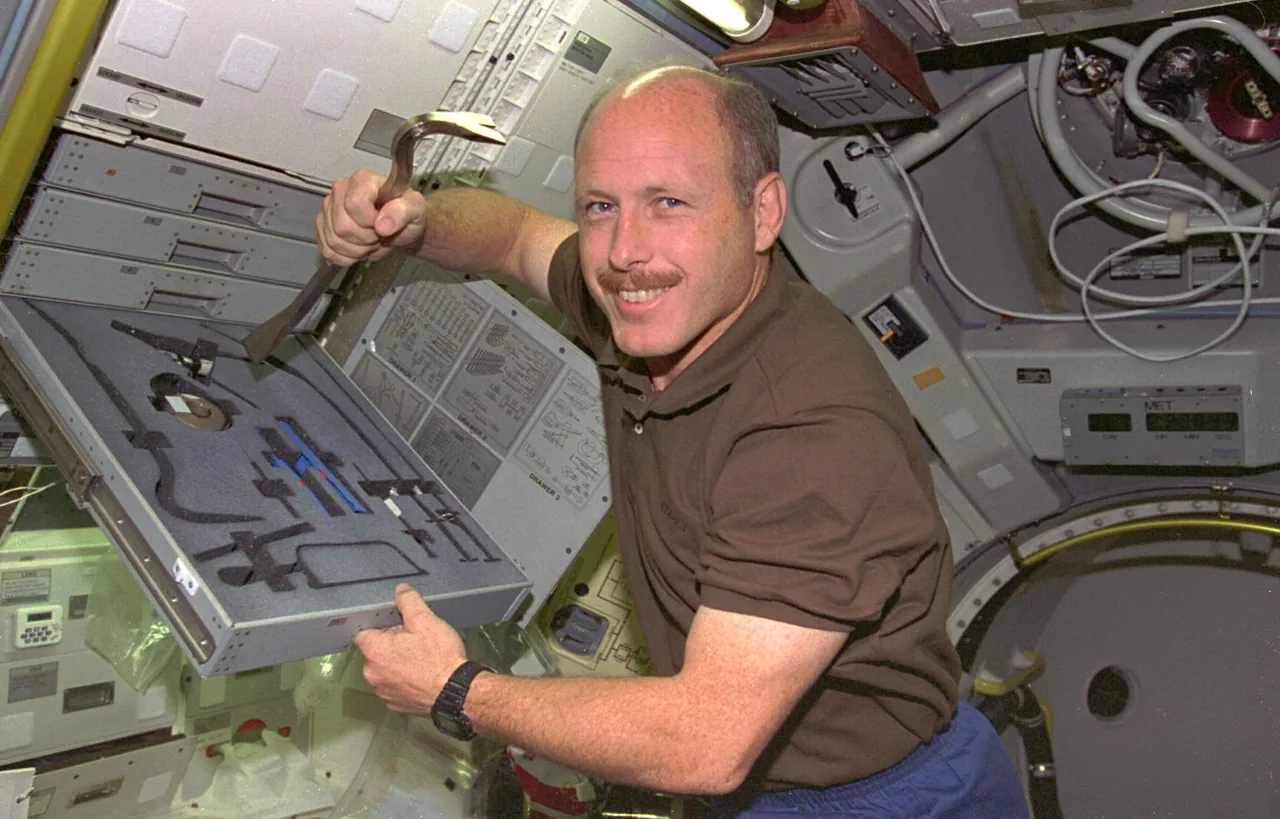 One STS-73 crew member holds a bent metal tool above an open foam-lined tool tray inside the laboratory module.