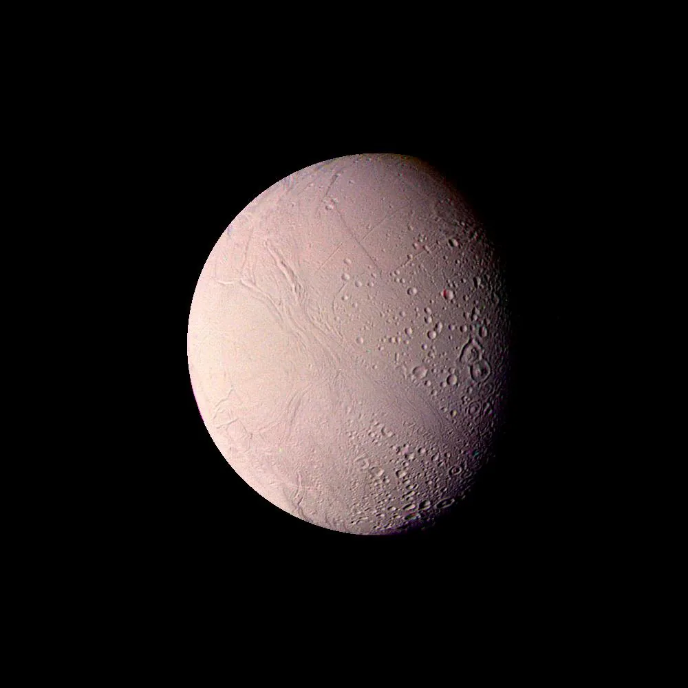 A pinkish Voyager mosaic of Enceladus shows smoother terrain toward the left and many resolved craters toward the darker right-hand limb.