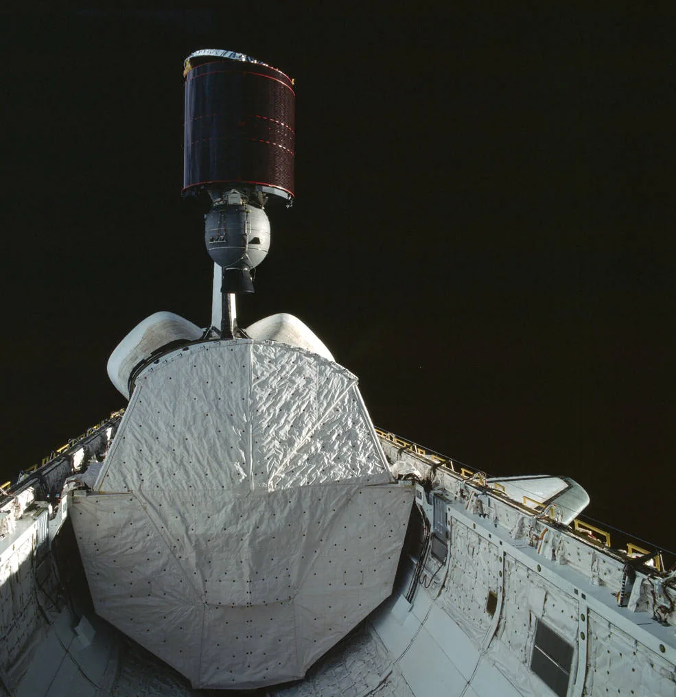 Cylindrical Anik C3 satellite and attached stage above Columbia’s open payload bay against black space