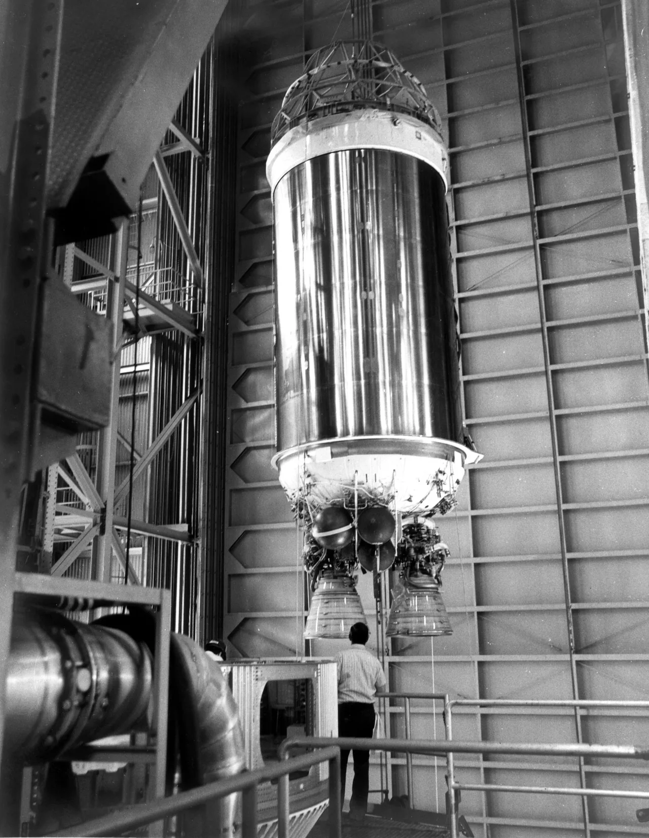 A tall Centaur D-1T upper stage hangs in an industrial building with two main engine bells beneath its tanks