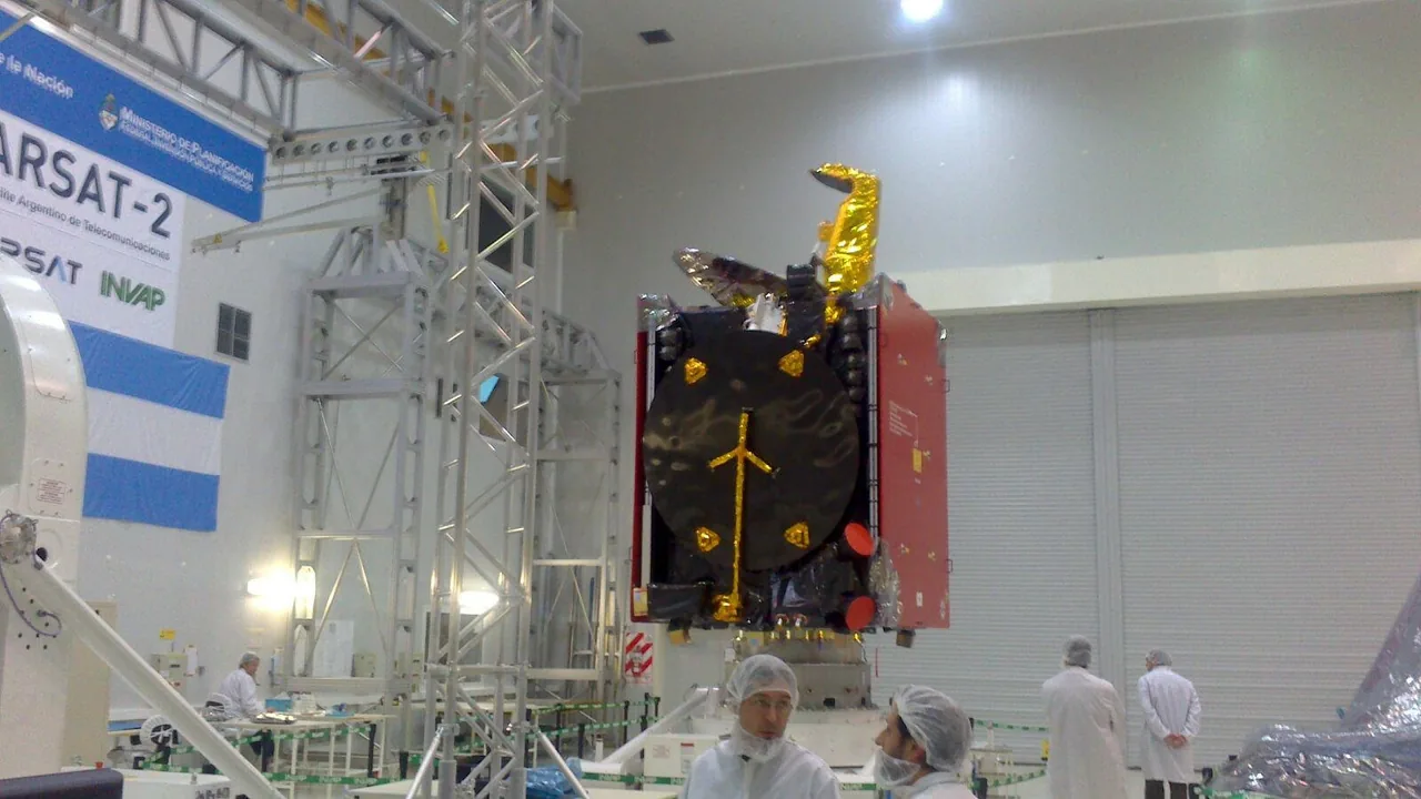 ARSAT-2 sits on a support stand in the INVAP cleanroom, with a dark circular face, red side panels and gold-covered fittings