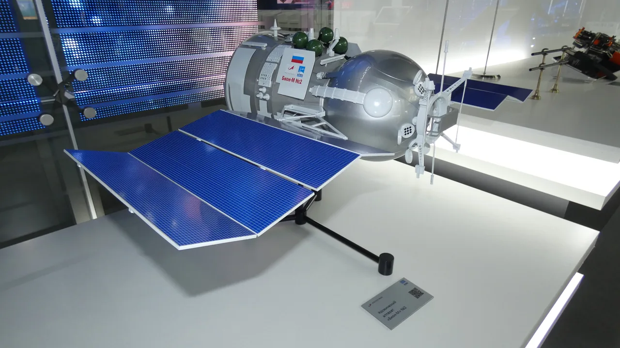 A silver Bion-M No. 2 display model with a spherical capsule and blue solar panels at an air show
