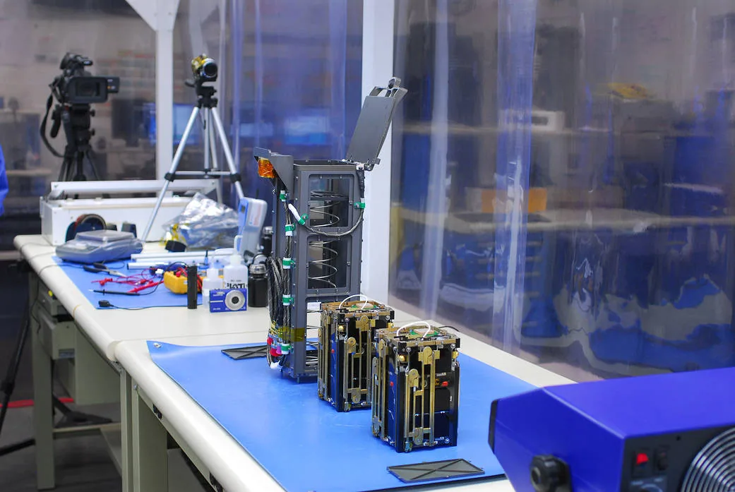 Two small DICE spacecraft sit beside their deployment hardware on a laboratory bench