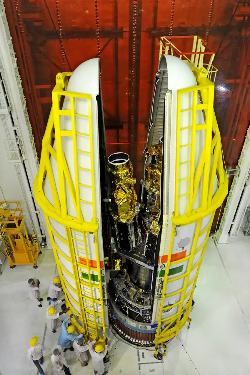 An overhead view into the opened PSLV-C28 fairing shows the tall gold-insulated DMC3 spacecraft mounted around the payload adapter, with technicians below.