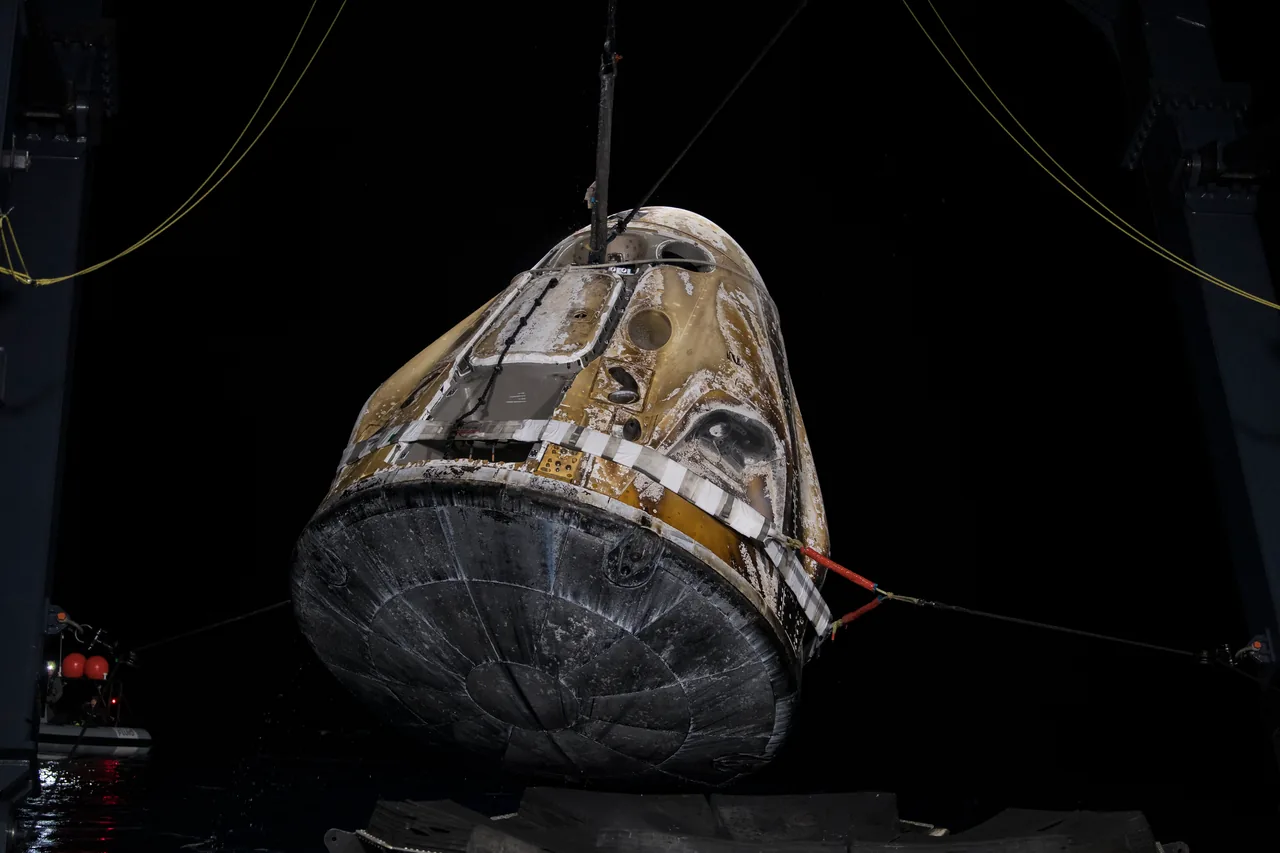 Dragon Endurance hangs from recovery cables at night, with its dark heat shield facing the camera