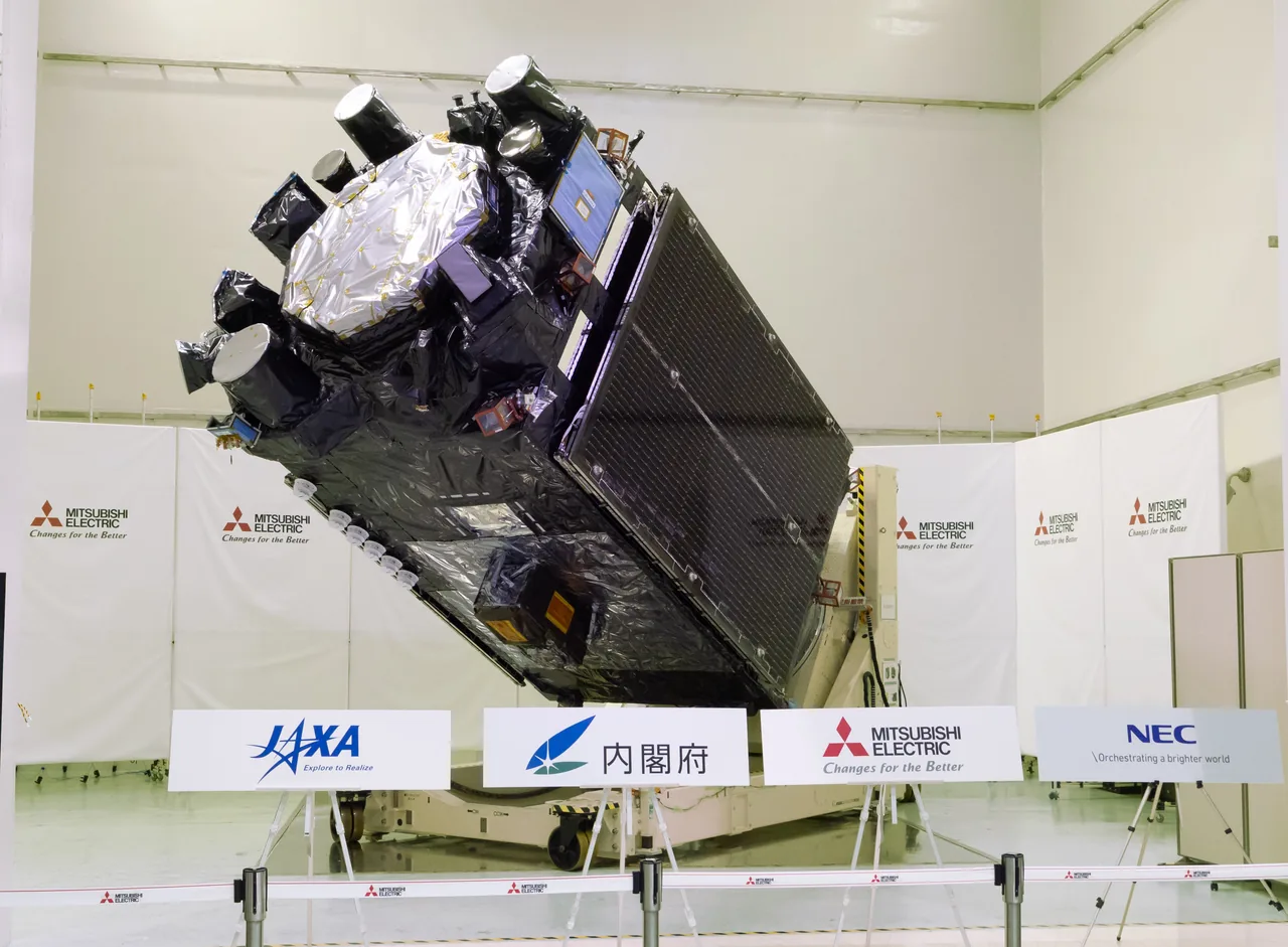 The Michibiki-7 flight satellite stands tilted on ground-support equipment in a clean room, showing its black thermal blankets, circular antenna faces, gold-covered central antenna, blue equipment panel, and a large stowed dark solar array.