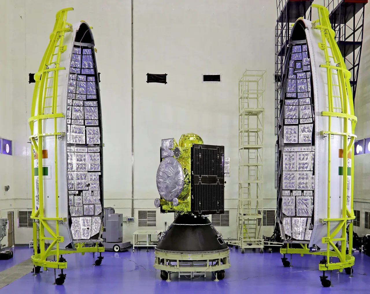 The gold-insulated NVS-01 spacecraft with a circular antenna and dark rectangular panel centered on a launch adapter between two tall opened payload-fairing halves.