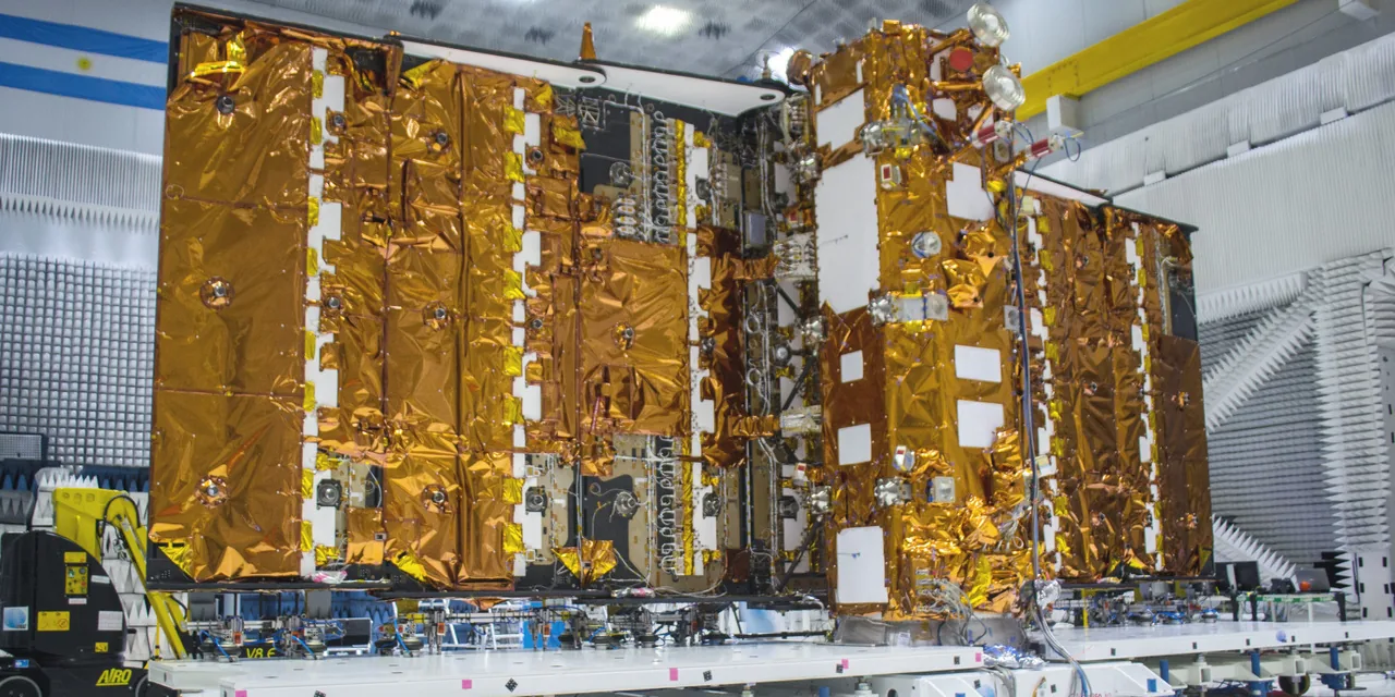 Wide test-facility photograph of the gold-foil-covered SAOCOM-1B spacecraft with its large rectangular radar antenna unfolded beside the spacecraft bus.