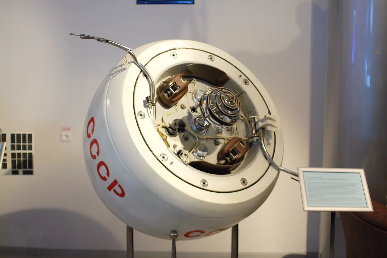 A white spherical Venera 4 capsule model stands in a museum with a large circular opening that exposes springs, wiring, and internal instruments.