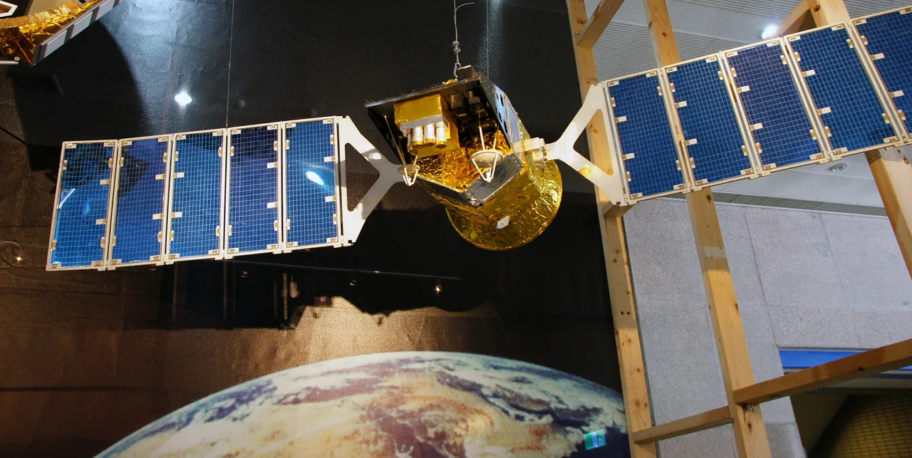 A gold-covered satellite display with two blue solar arrays hangs above an Earth mural