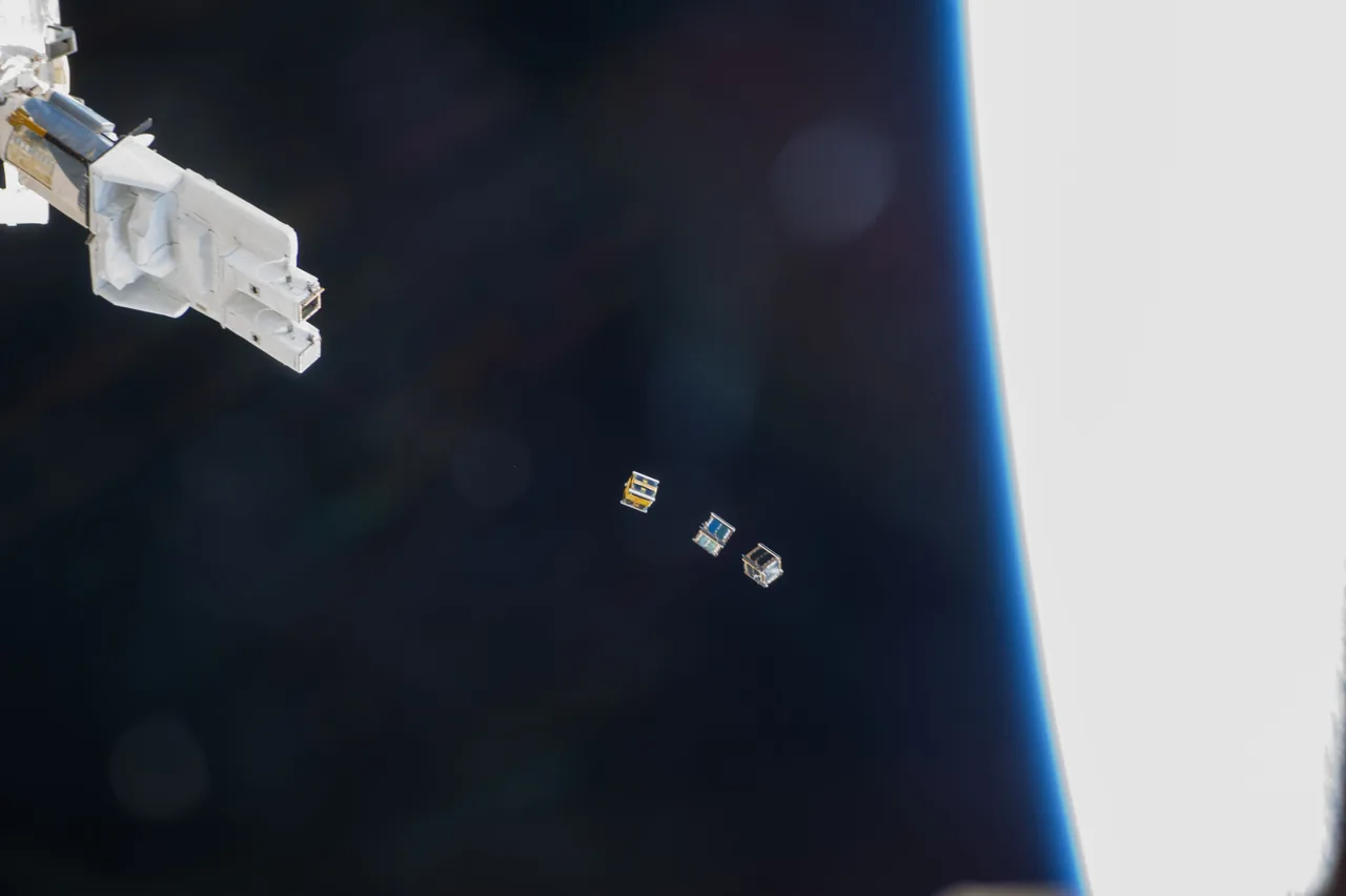 Three small CubeSats drift away from a station-mounted deployer beside Earth’s bright blue-edged limb