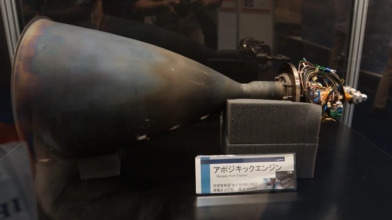 A large bell-shaped engine nozzle lies horizontally in a museum exhibit beside a labeled display card