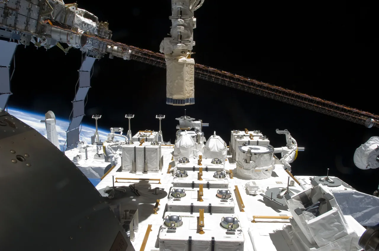 White experiment pallets and fixtures covering Kibo's Exposed Facility, with the station truss and Earth beyond.