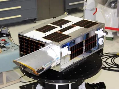 NEOSSat on a laboratory turntable, with its long open telescope baffle projecting from the solar-panel-covered spacecraft