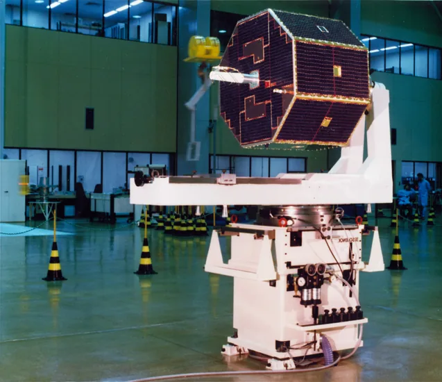 Octagonal SCD-1 satellite covered in dark solar cells above a large white handling fixture in a laboratory