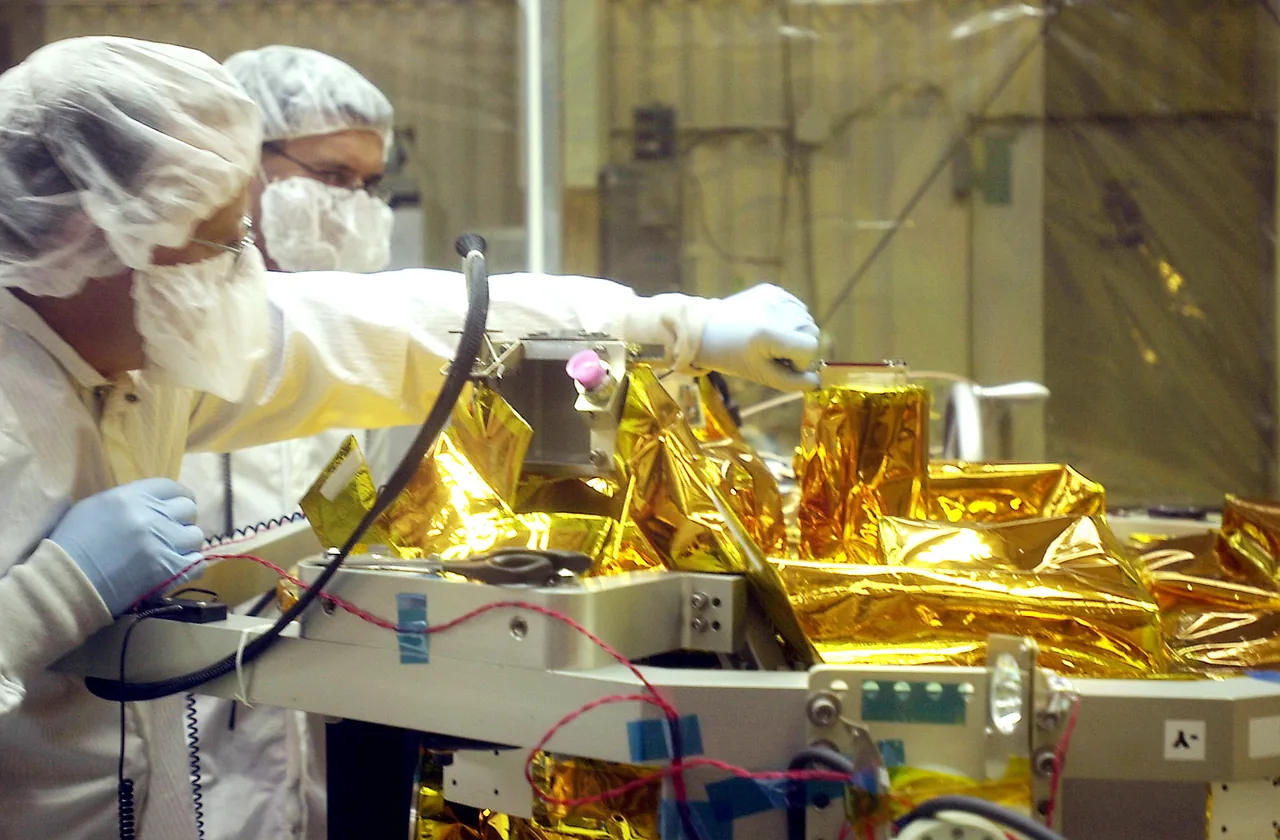 Two technicians in cleanroom clothing working beside gold-covered SCISAT hardware and connected test cables.