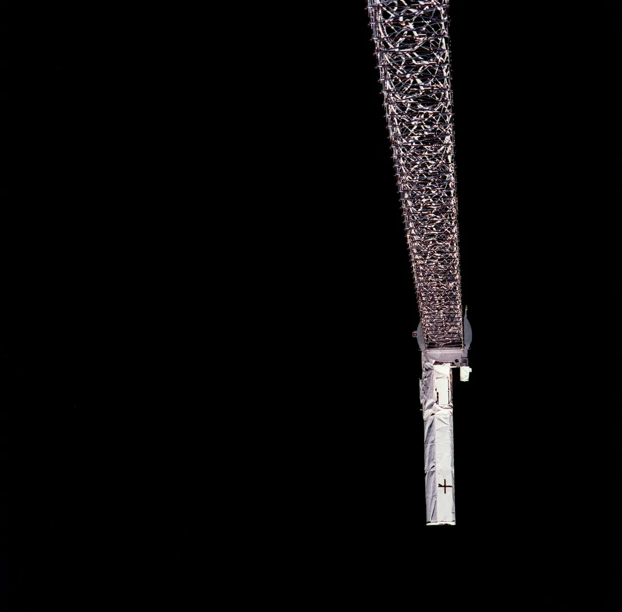 A silver lattice mast extends down from the frame’s upper edge to a long pale antenna against black space