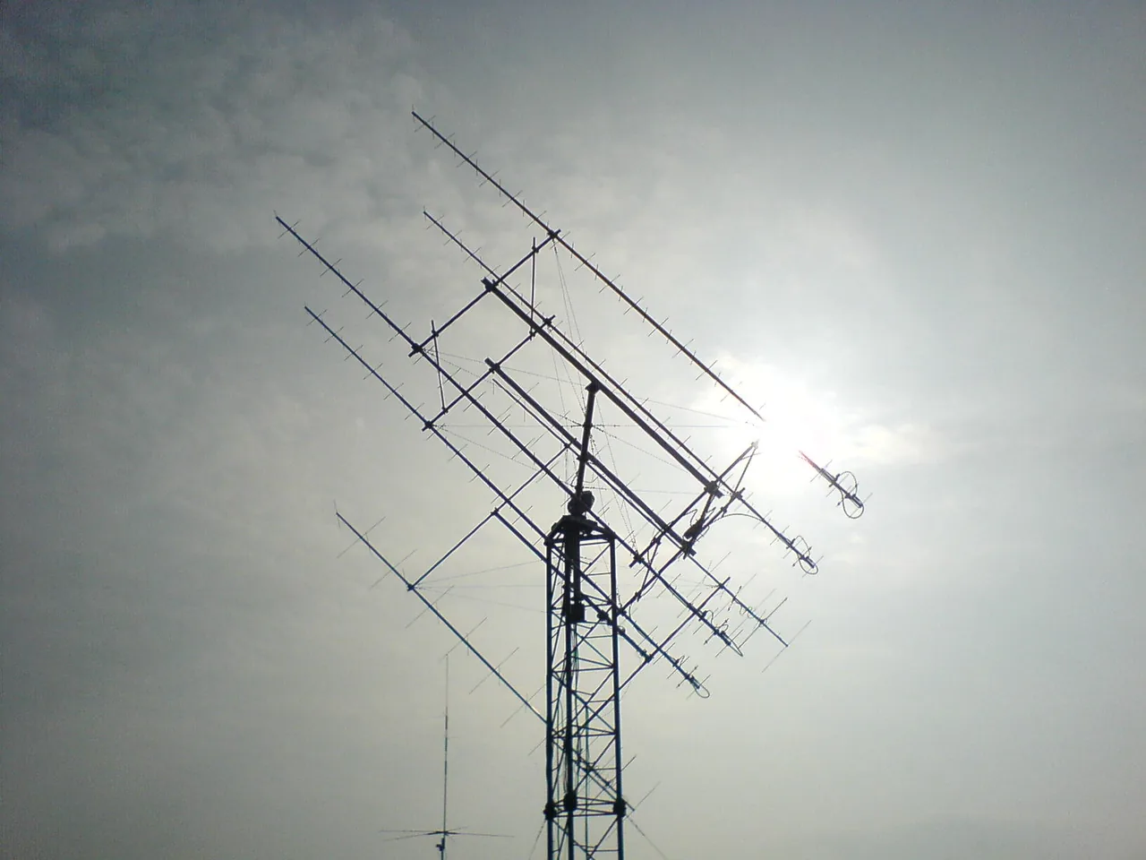 Crossed directional antenna arrays extend from a mast against a partly cloudy sky