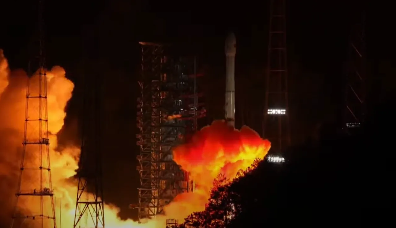 A rocket ignites at night beside a service tower, with bright orange exhaust and trees in the foreground.