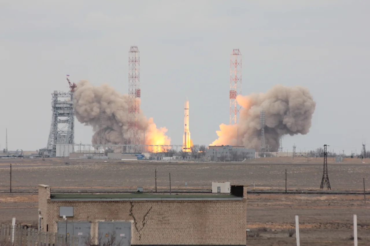 A Proton rocket rises above its launch pad on a bright exhaust plume against a pale blue sky