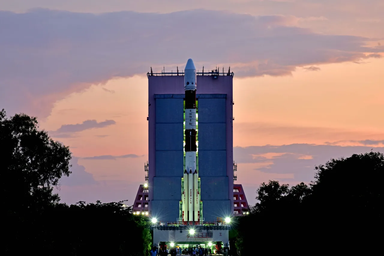 A PSLV rocket stands beside its tall service structure under a pink twilight sky