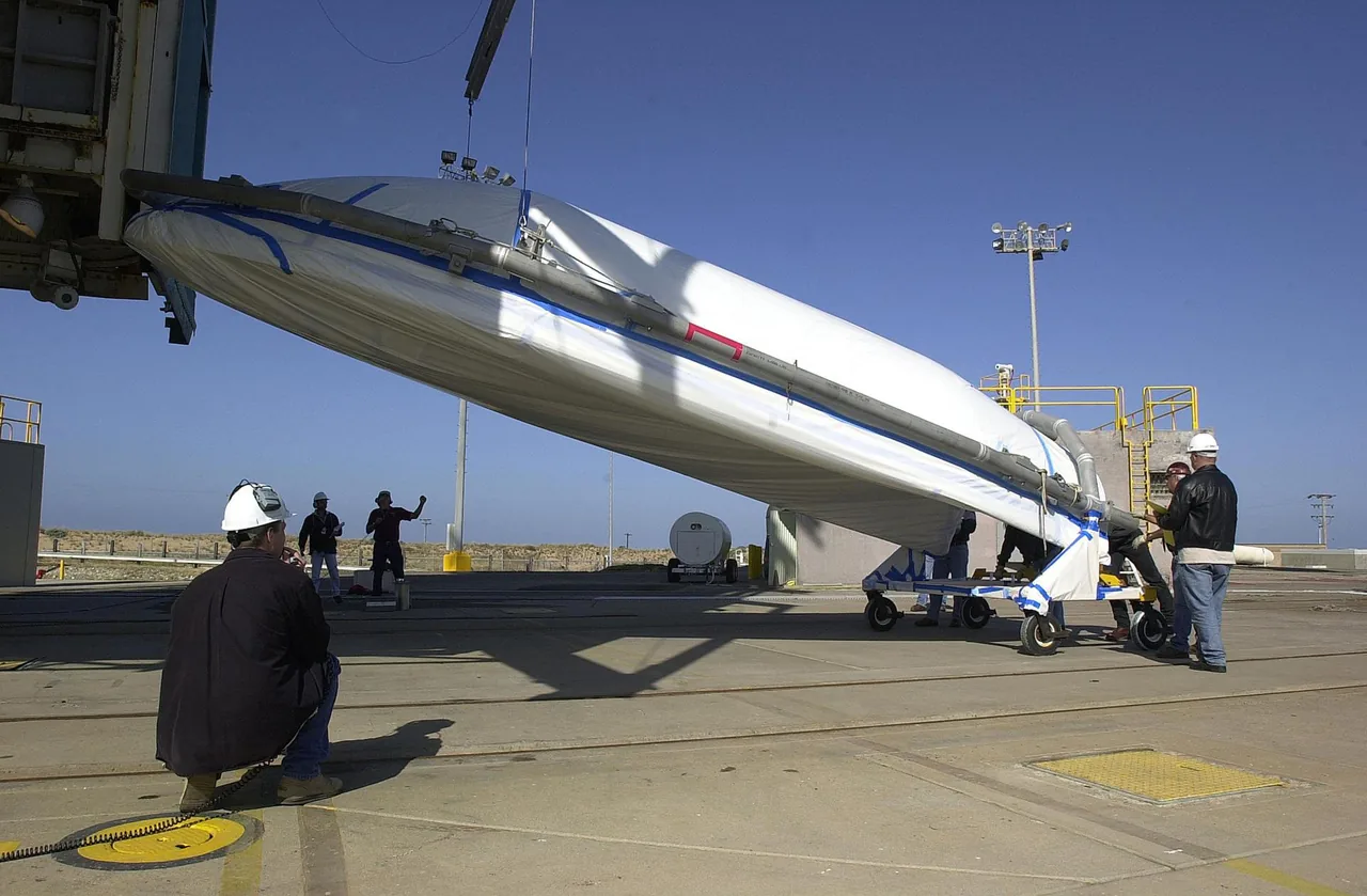 Workers guide a large curved payload-fairing section as it is lifted beside launch facilities