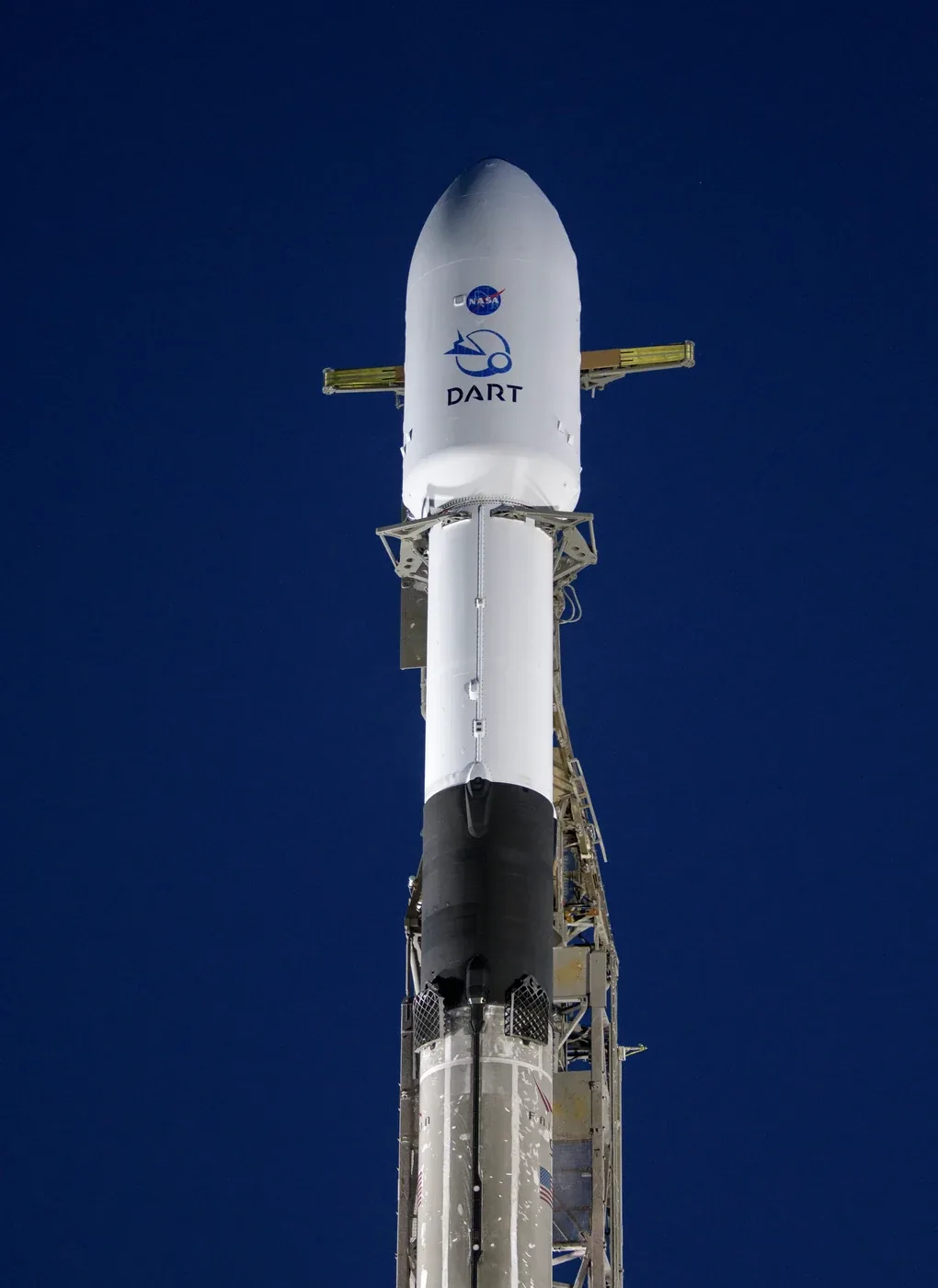 A Falcon 9 rocket with DART markings stands on the pad against a dark blue dawn sky