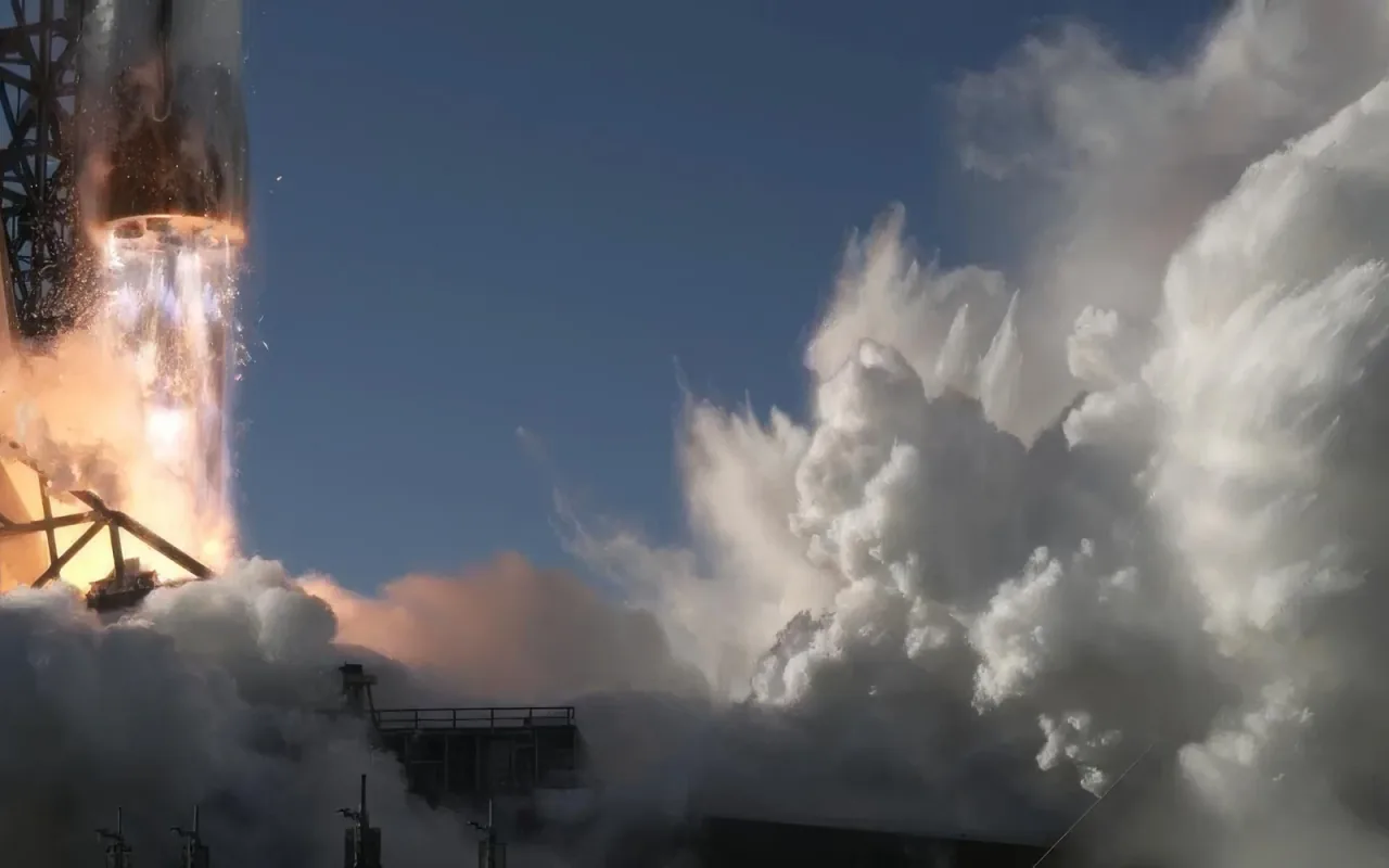 The lower portion of a New Glenn rocket rises beside its tower amid bright exhaust and dense white clouds