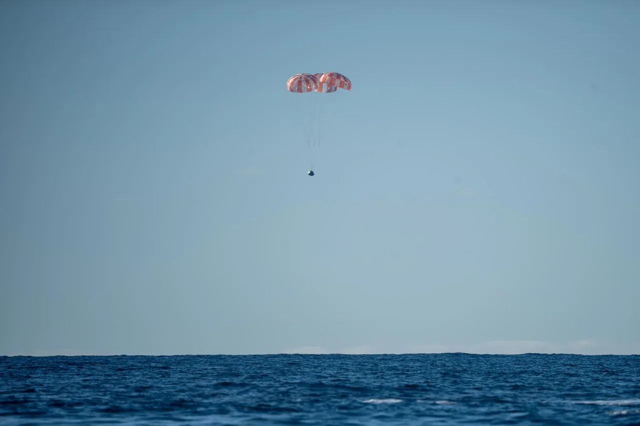 Orion descends beneath three orange-and-white parachutes over the Pacific
