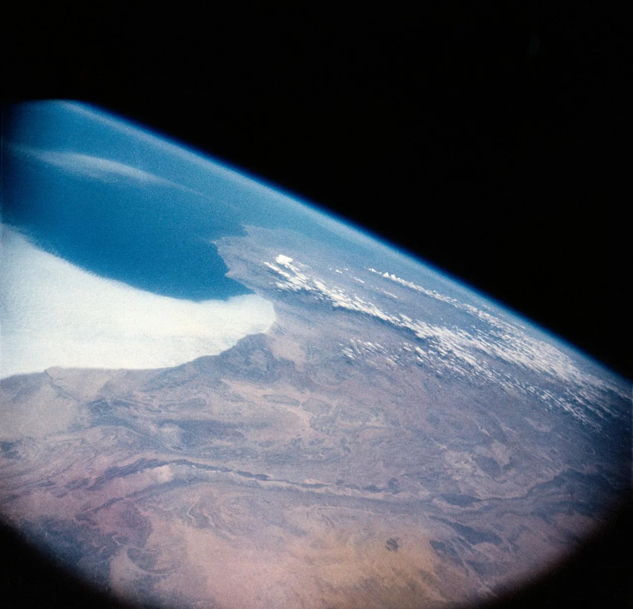 Earth’s curved horizon with blue atmosphere, clouds and land