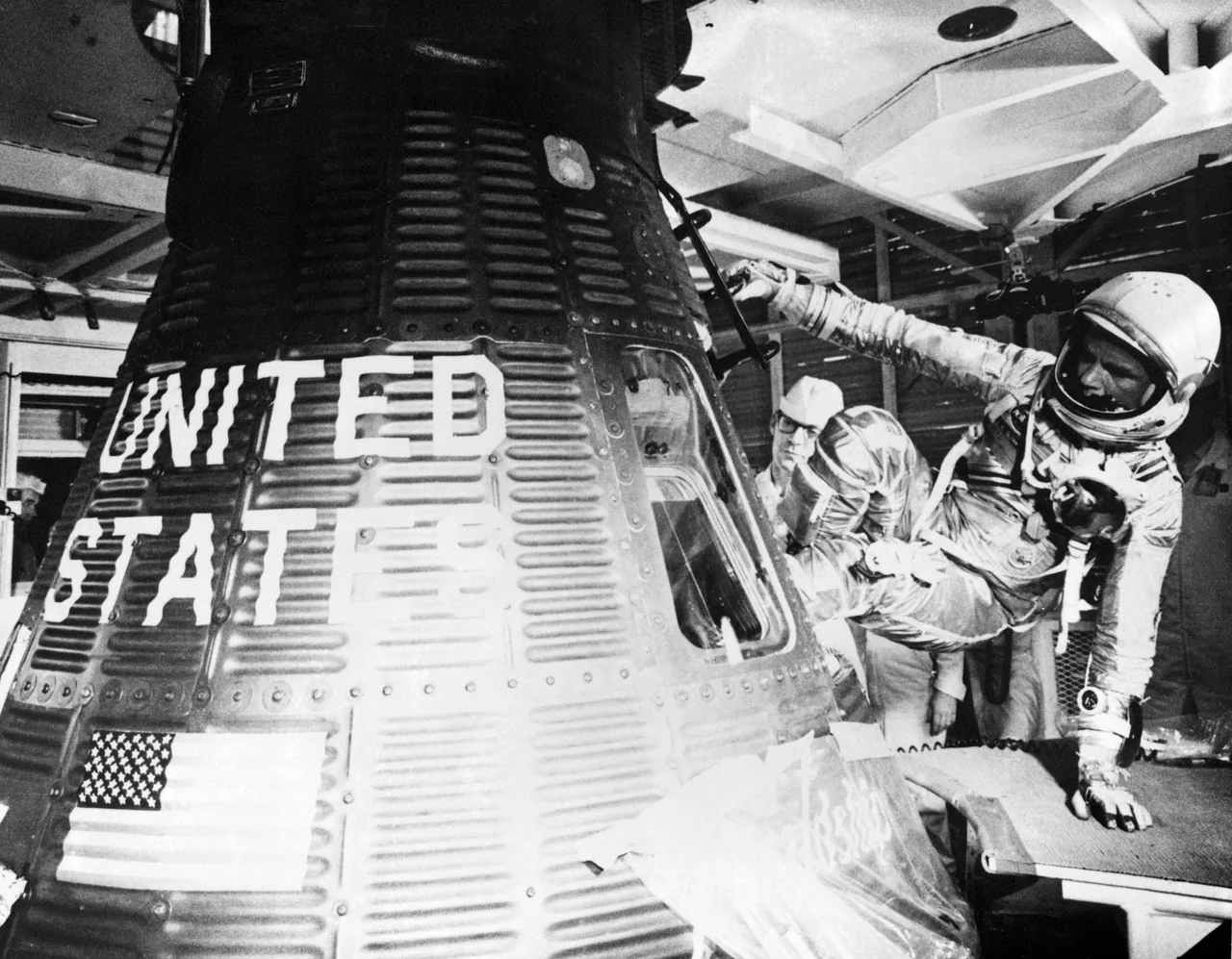 John Glenn in a pressure suit entering Friendship 7 while technicians assist beside its open hatch