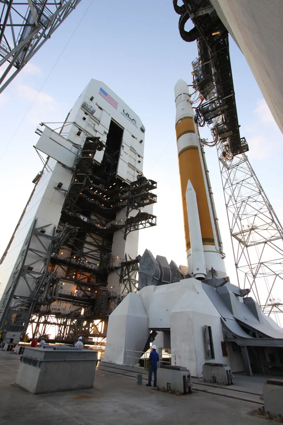 A white-and-orange Delta IV rocket stands beside a retracted service structure under a blue sky
