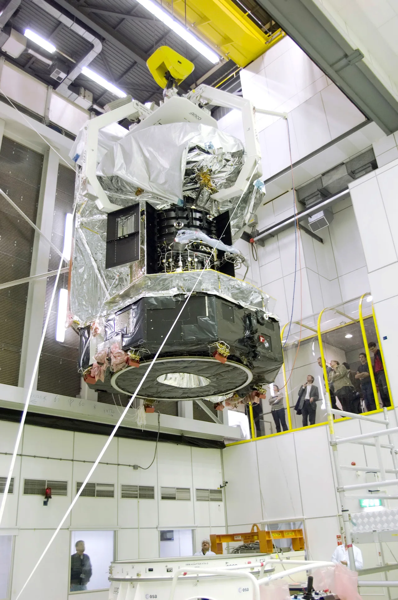 A large foil-covered observatory hangs high in a cleanroom above workers and an open test area.