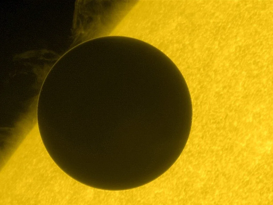 Dark disk of Venus silhouetted against the bright yellow-rendered solar limb, with fine solar texture visible around it.