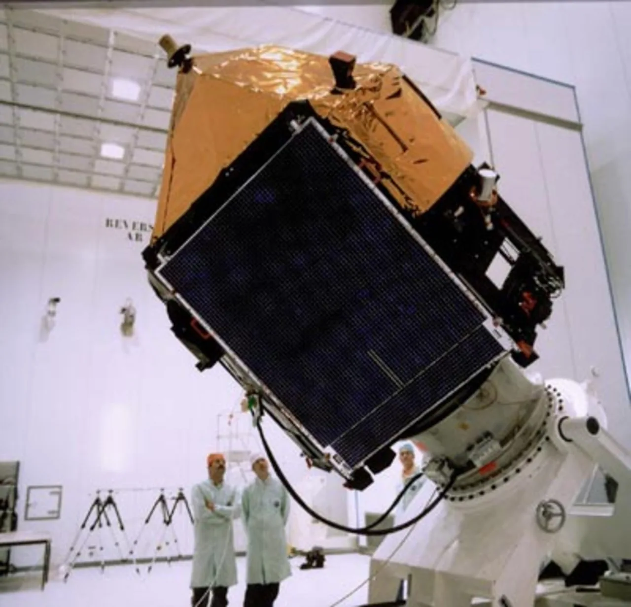 Hipparcos is tilted on a large test fixture, its dark solar panel in front of a gold-covered body and technicians nearby.