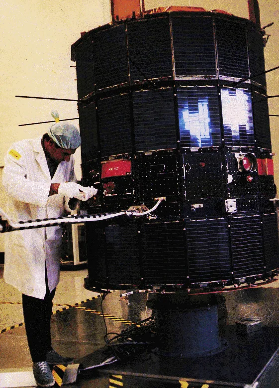 A technician works beside IMP-8’s tall dark solar-cell-covered cylindrical body