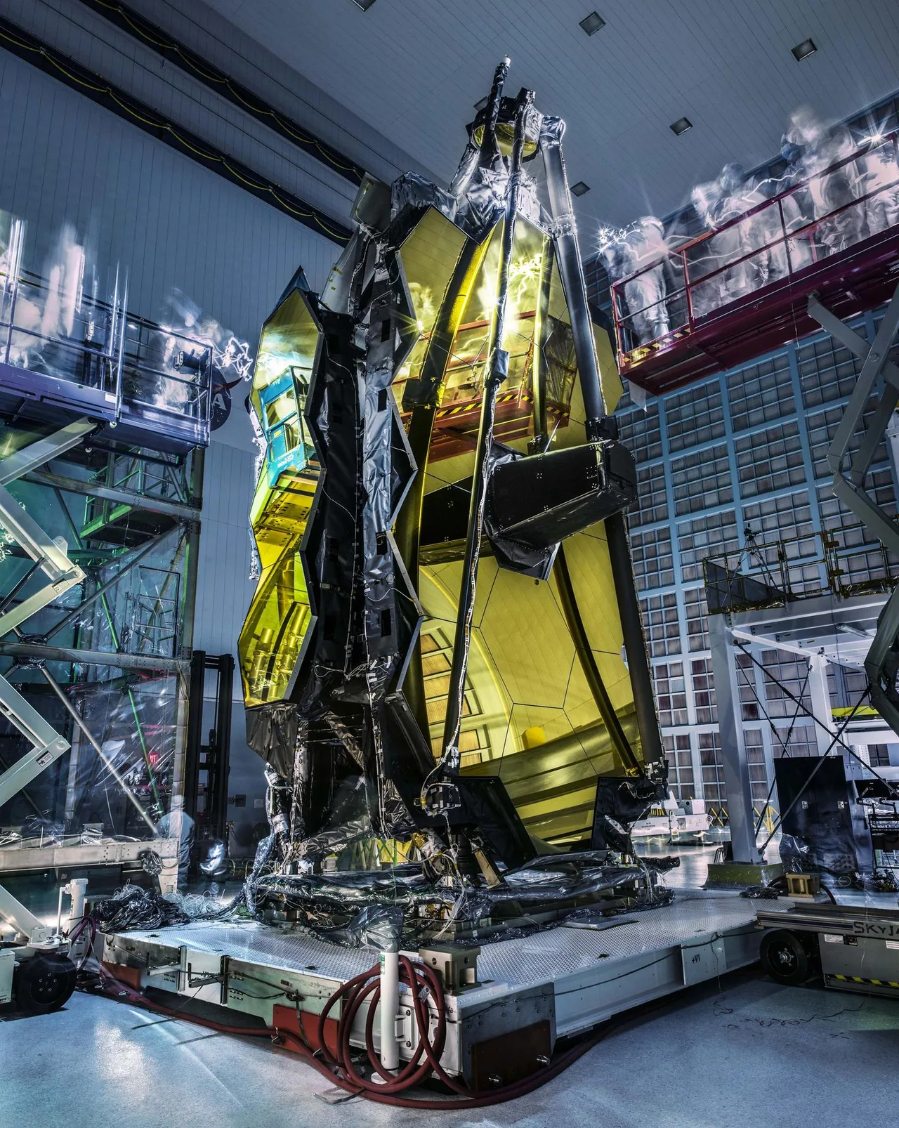 Webb’s gold-colored segmented mirror during a darkened clean-room inspection, with blurred technicians and light trails