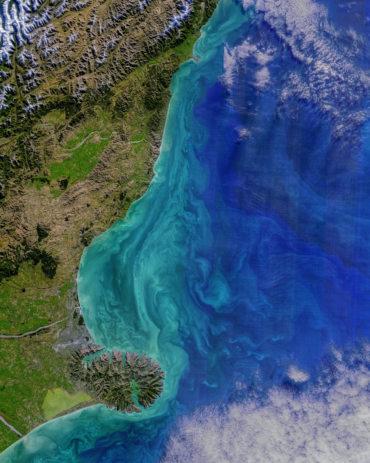 Landsat view of the Canterbury coast with turquoise sediment patterns offshore, rivers crossing plains, Banks Peninsula and mountain terrain