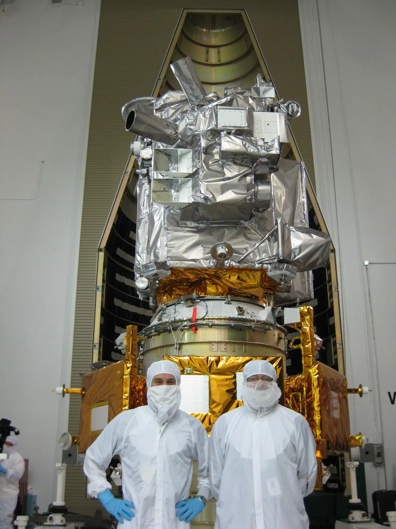 Two team members in clean-room clothing stand before the stacked LRO and LCROSS spacecraft at a preflight media event