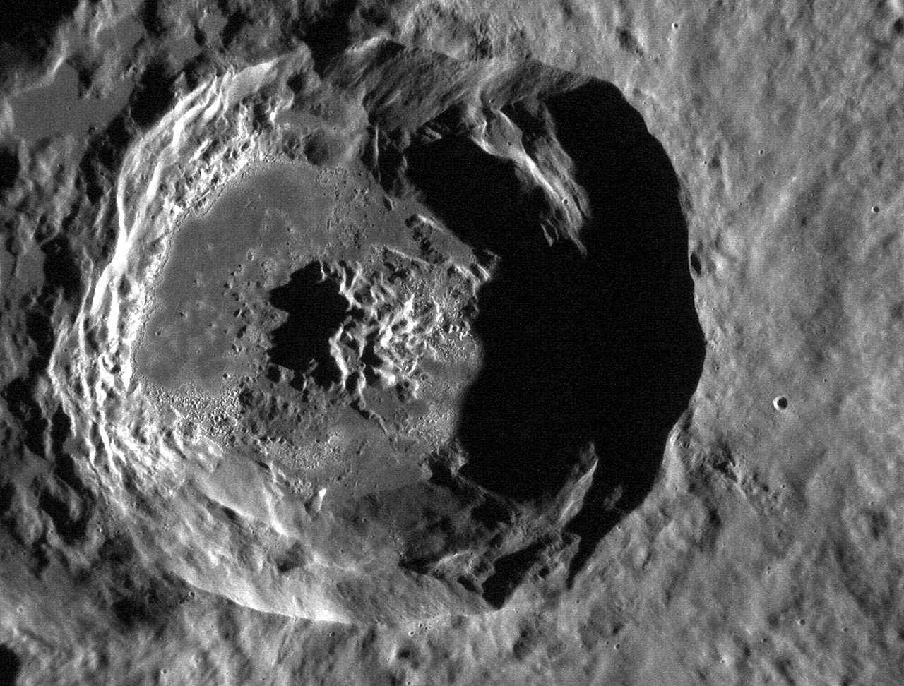 A grayscale Mercury crater has a bright left rim, a strongly shadowed right interior, and irregular etched patches across its floor.
