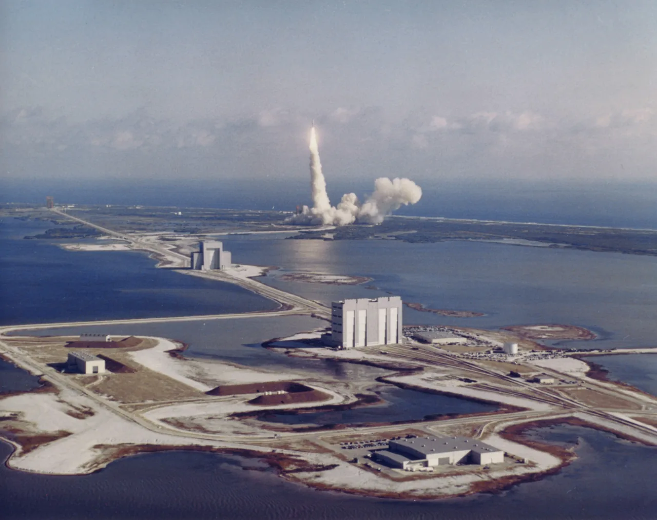 An aerial view shows the Titan IIIC launch plume beyond roads, waterways and launch facilities
