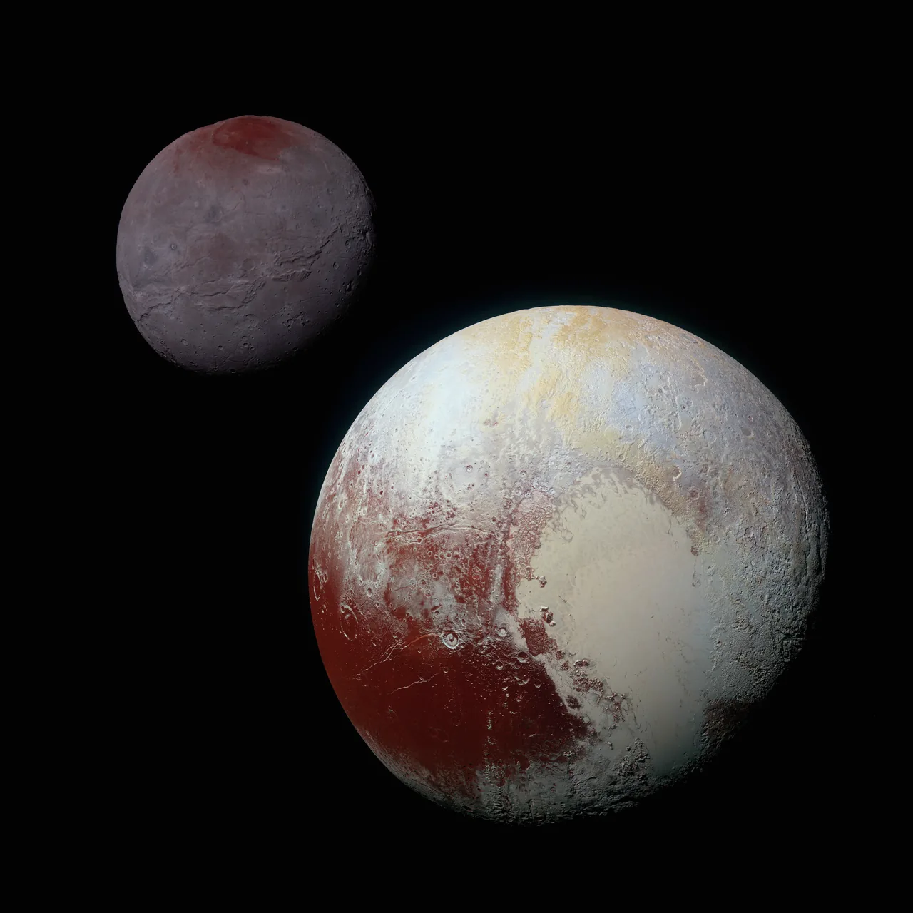 Pluto’s large pale and reddish globe appears at lower right, while smaller gray Charon with a reddish polar region is placed at upper left against black.