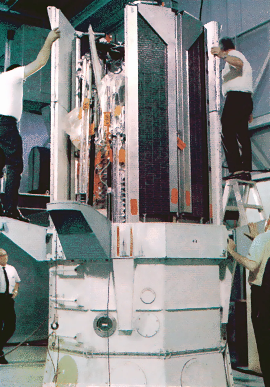 Technicians assemble OGO-6 beside large rectangular panels in a ground facility