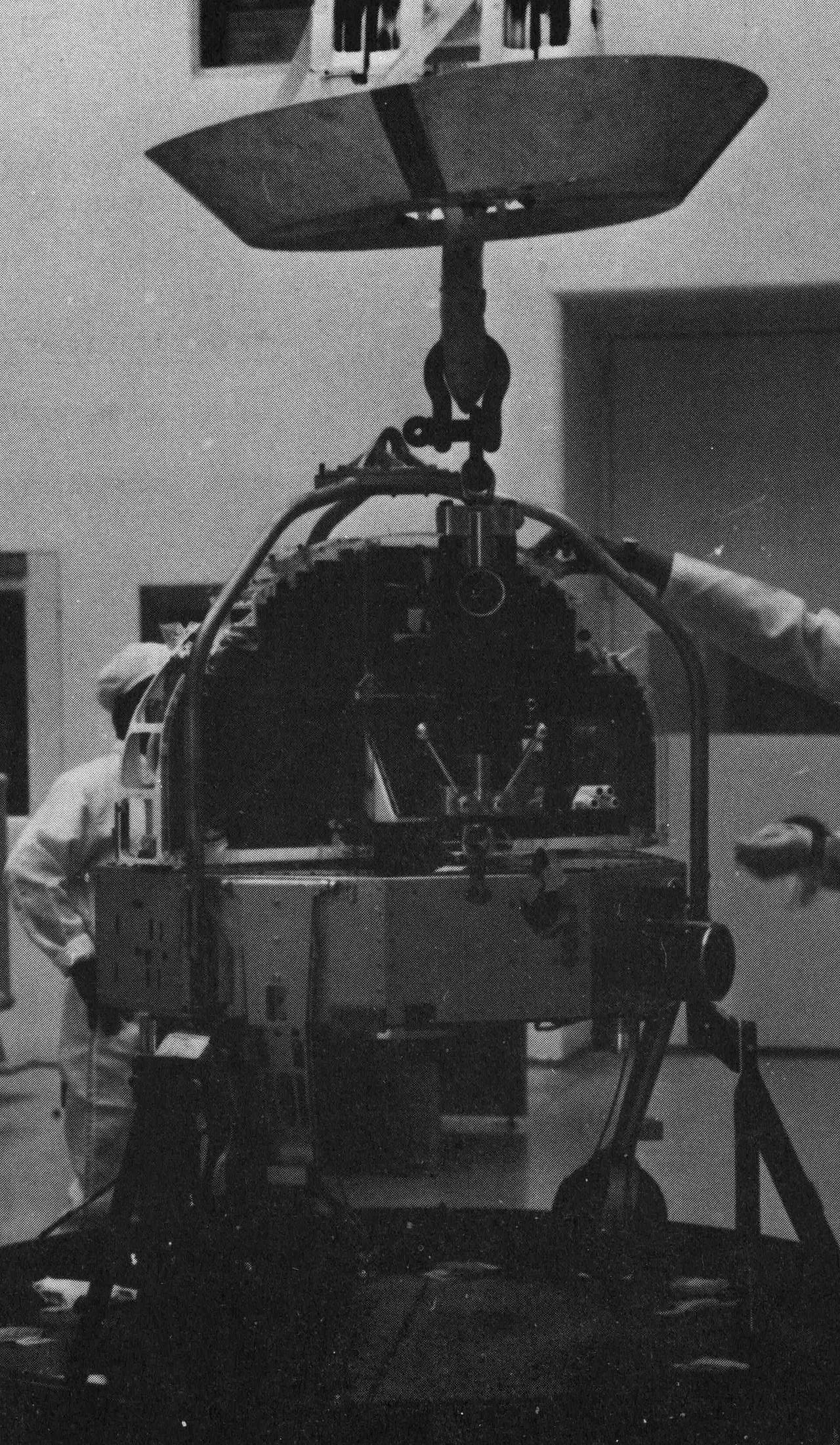 Black-and-white view of OSO-6 suspended beneath lifting equipment during preparation