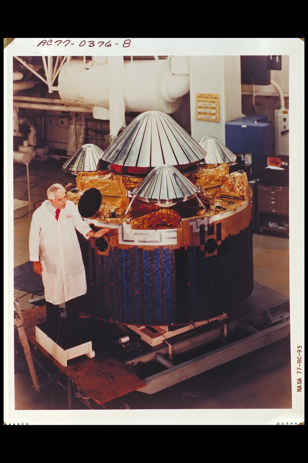 A person in a white coat stands beside Pioneer Venus multiprobe hardware, with one large and three smaller cone-shaped probe assemblies on a cylindrical carrier.
